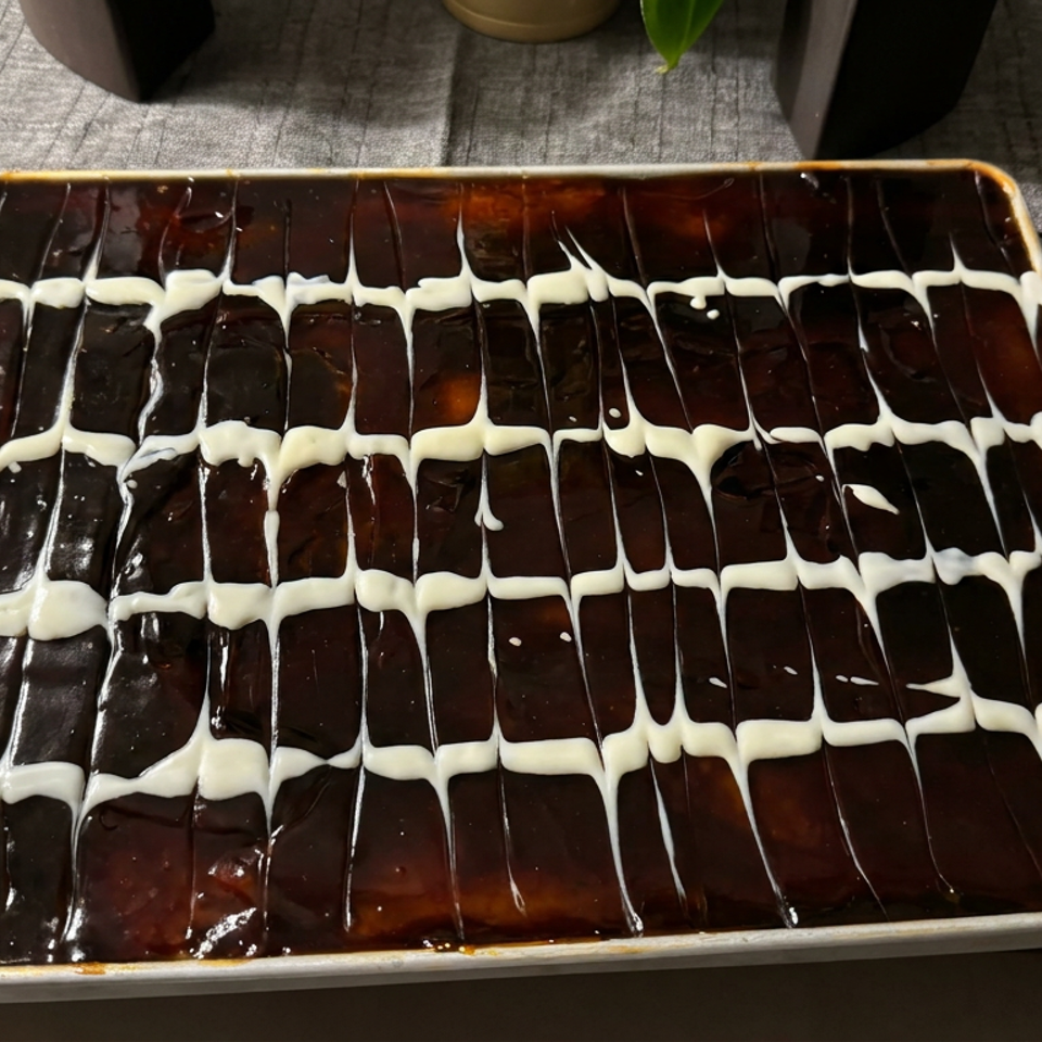 Rectangular tray of glossy chocolate dessert decorated with white icing in a feathered grid pattern.