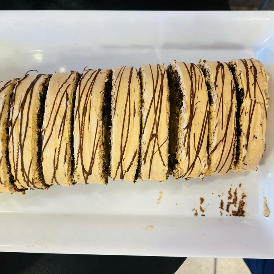 Sliced cream-filled pastry roll drizzled with chocolate on a white rectangular plate.