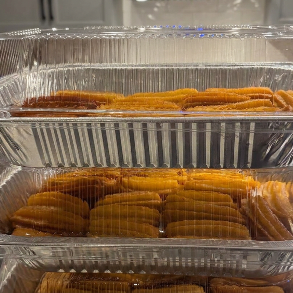Three stacked aluminum trays hold rows of golden fried pastries in a bright kitchen.